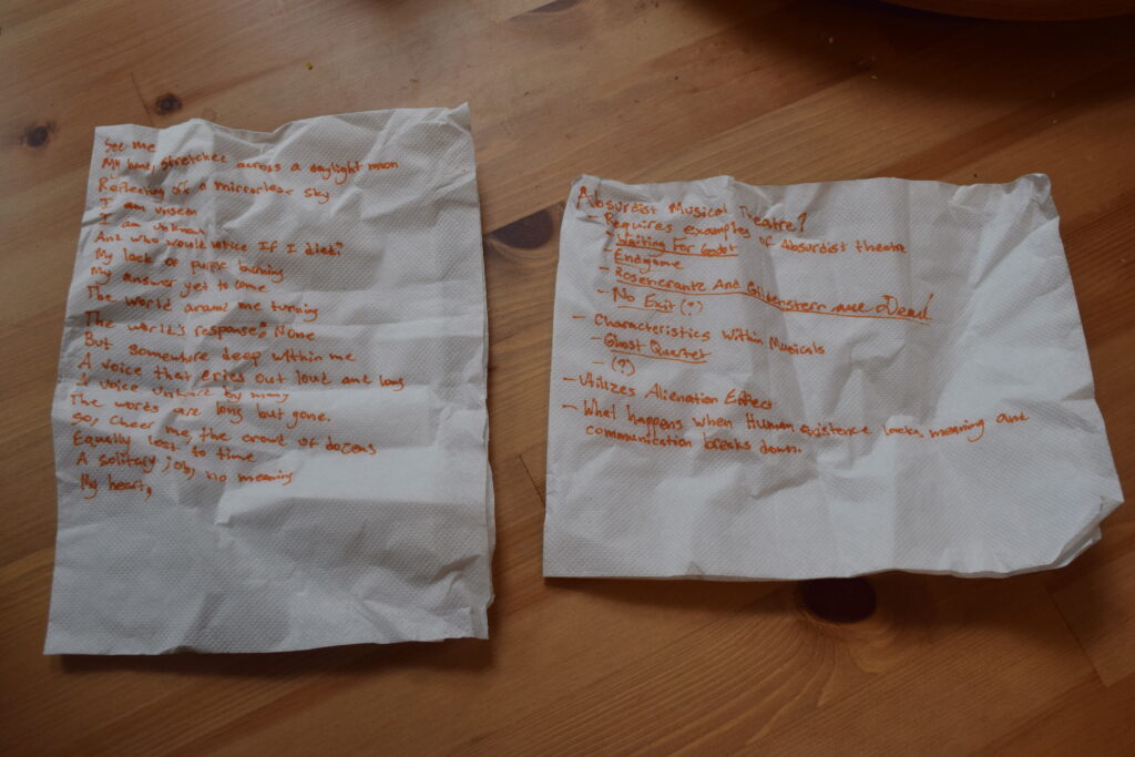 Two napkins with orange text: the left, a free-verse poem, the right, ideas on Absurdist Musical Theatre